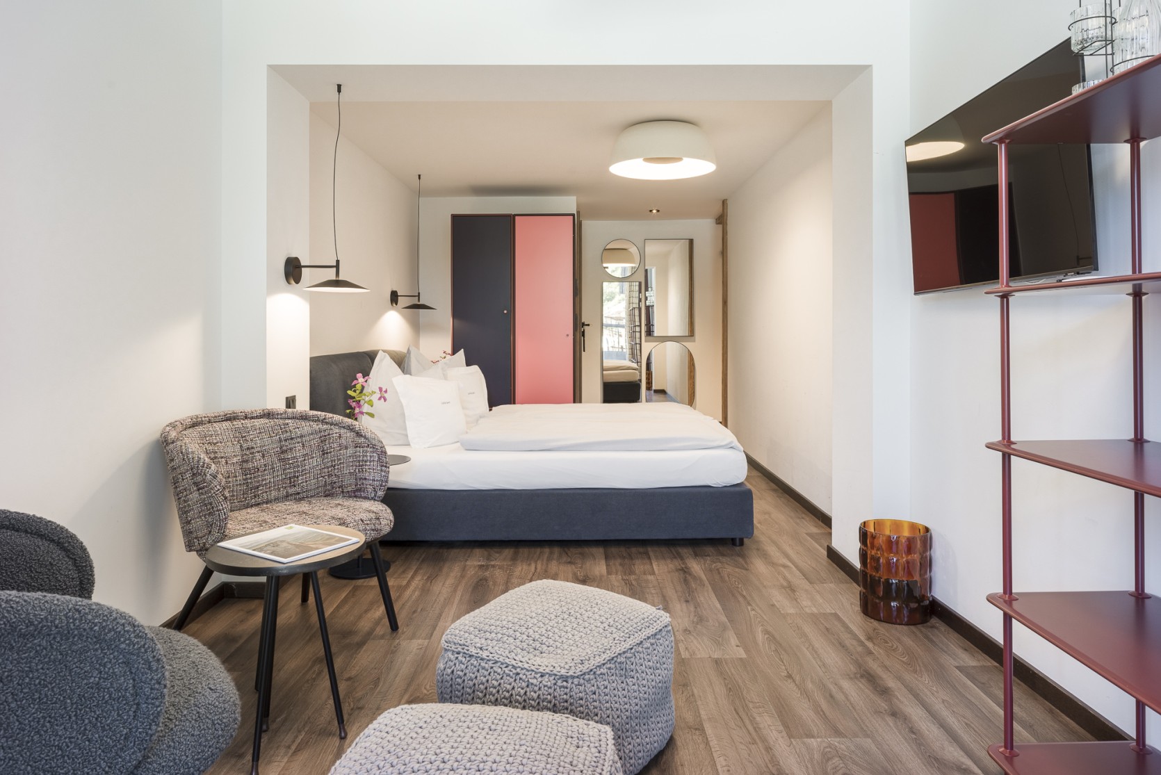 Modernes Doppelzimmer mit Sitzecke und rotem Metallregal im Breitach Hus Kleinwalsertal.