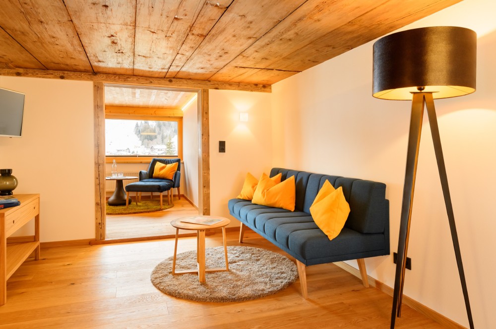 Cozy accommodations in the Kleinwalsertal valley, featuring a reclaimed wood ceiling, a blue sofa, and a floor lamp at the Breitach Hus.